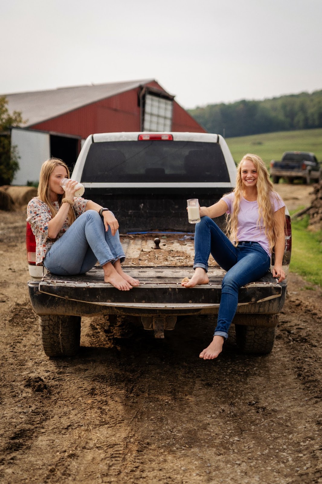 Two young girls drinking milk in the back of a truck at a farm
